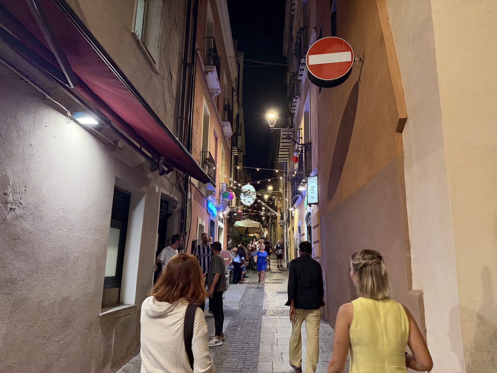 Cami and Lore walking up a narrow lane in Cagliari at night under strings of café lights