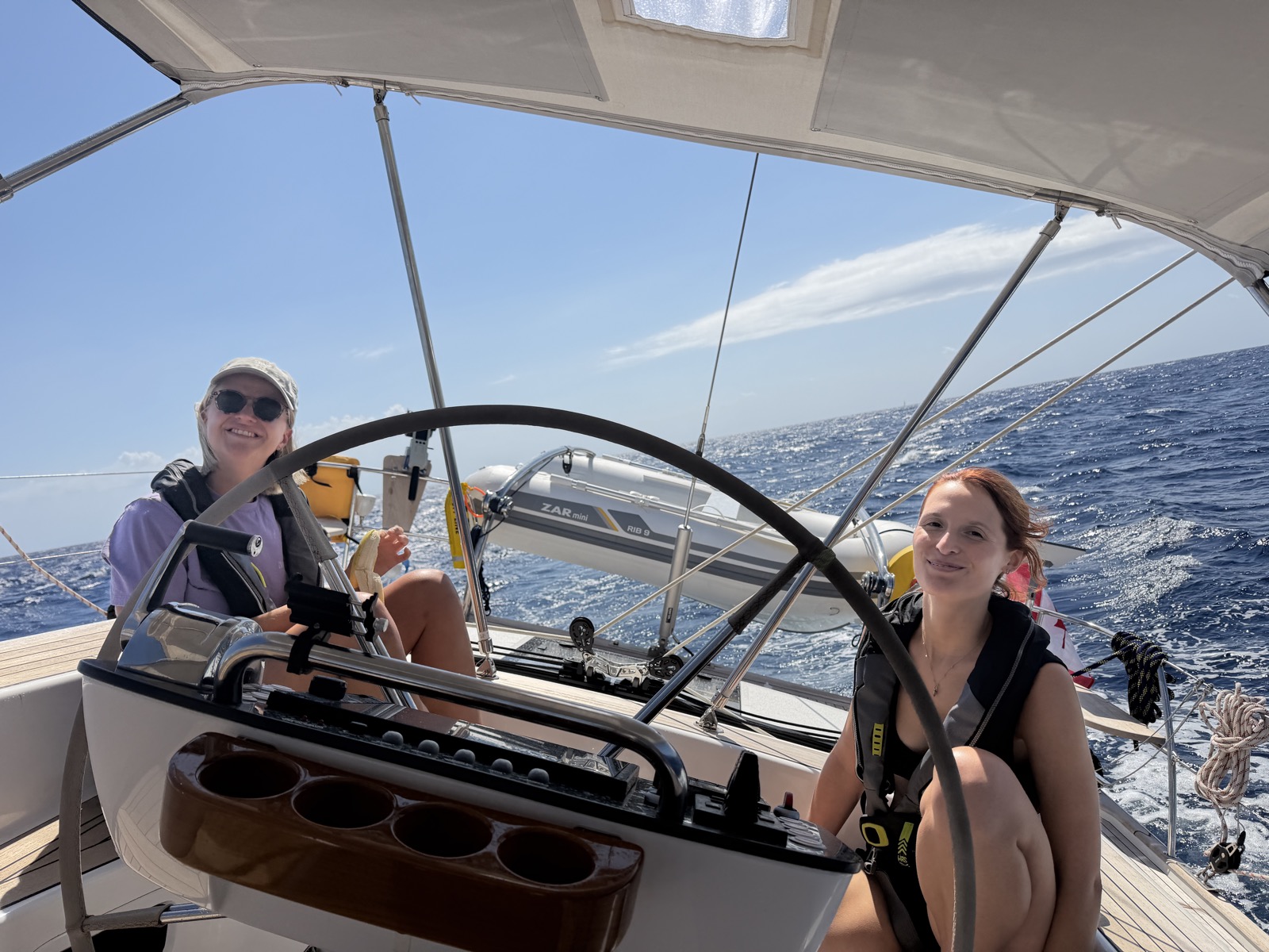 Cami and Lore smiling behind the wheel under the bimini on the sail from Gozo to Sicily