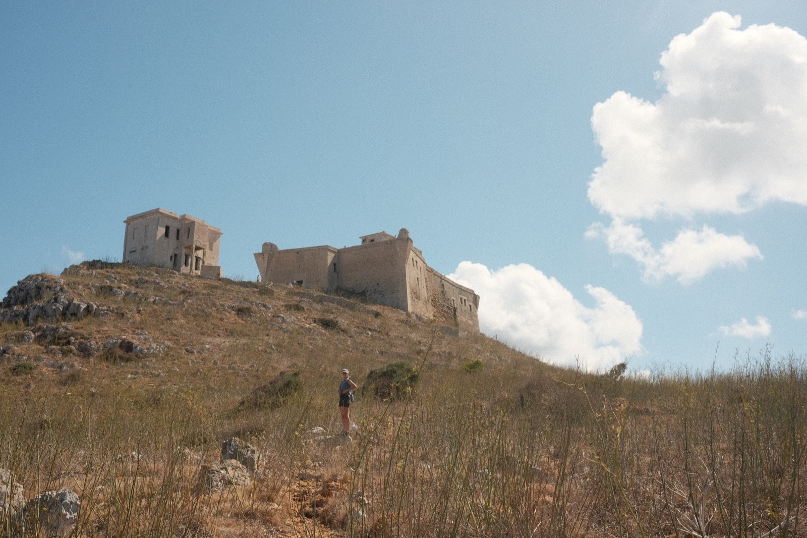The abandoned castle on the hilltop above Favignana, with a hiker in the grass below