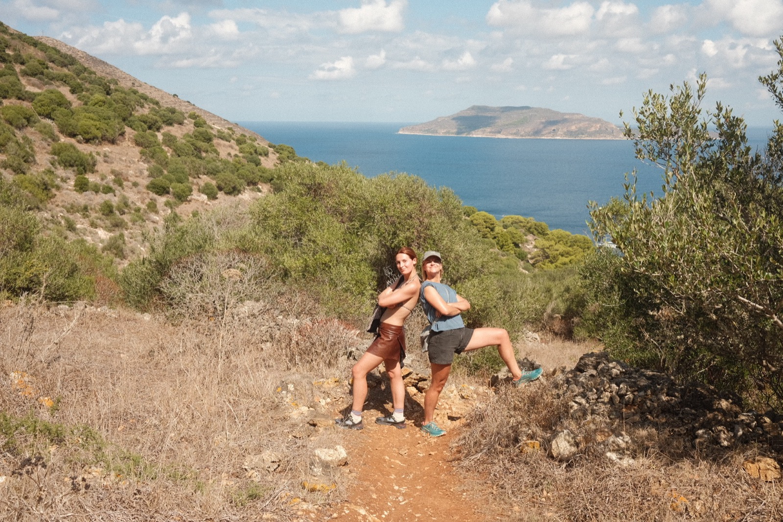 Cami and Lore posing back to back on the trail, with the sea and a neighbouring island behind them
